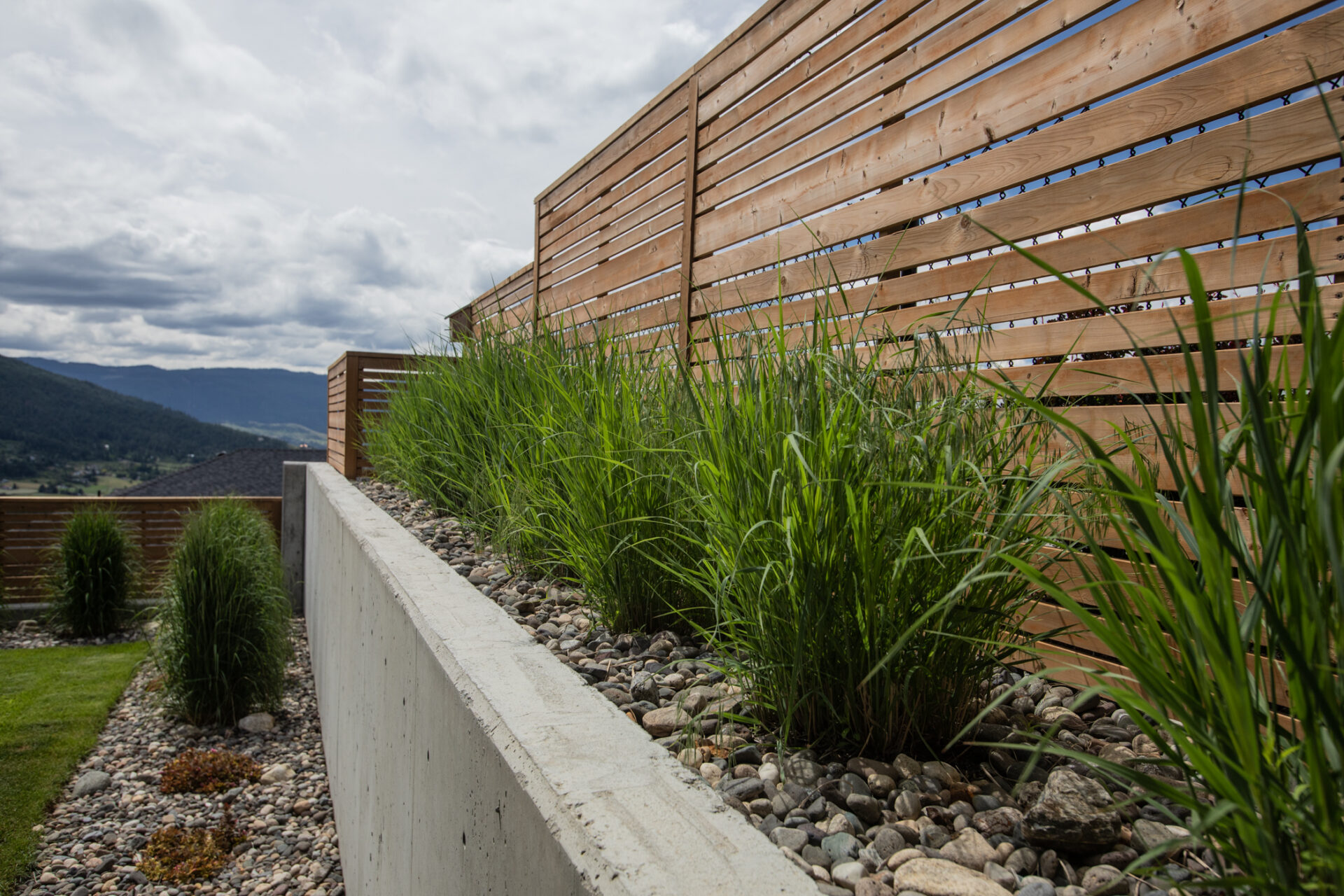 a brown slat fence with rock and greenery landscaping